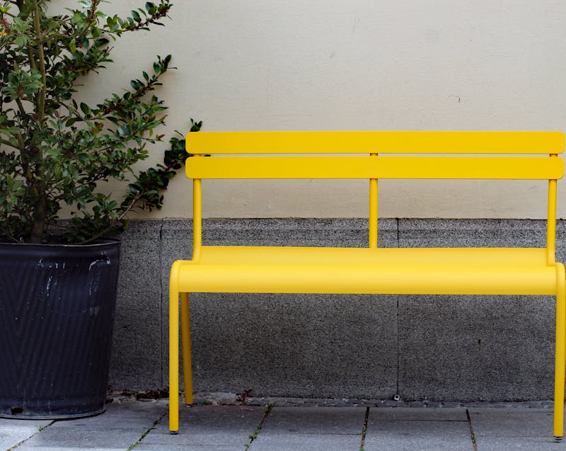 a plant, a bench, brick flooring, and a concrete wall